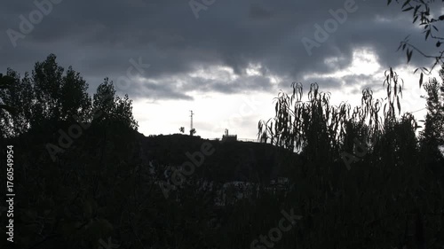 Time lapse in a field in southern Spain, with green-leaved trees, some buildings, and a cloudy sky.