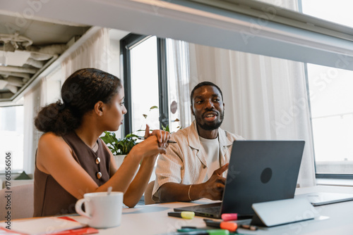 Quadro su tela A male worker is talking to a female worker who is sitting next to him at the ta