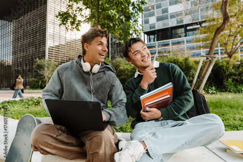 Fotografie Two male students sit and laugh while looking in the direction one of them is po