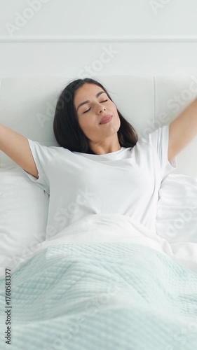 Feel the refreshing start of a new day as a person awakens, stretching and enjoying a moment of calm in bed.