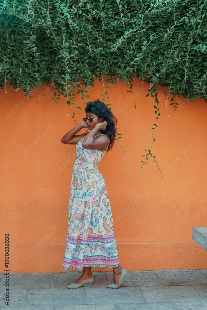 Fototapeta premium A woman in a white dress stands in front of a wall with green vines