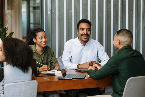 Female and male employees sitting at a table and smiling while listening to the male employee sitting across from them