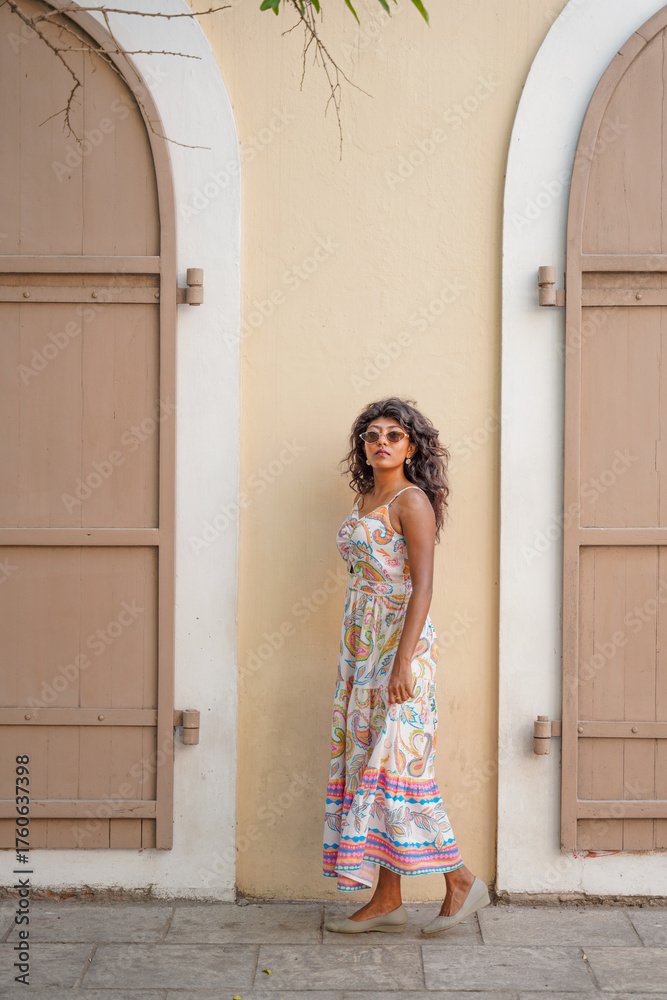 Fototapeta premium A woman in a white dress stands in front of a building with a tan wall