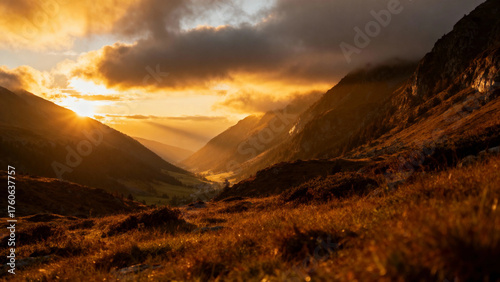 Golden sunrise illuminates a mountain valley with dramatic clouds and warm light
