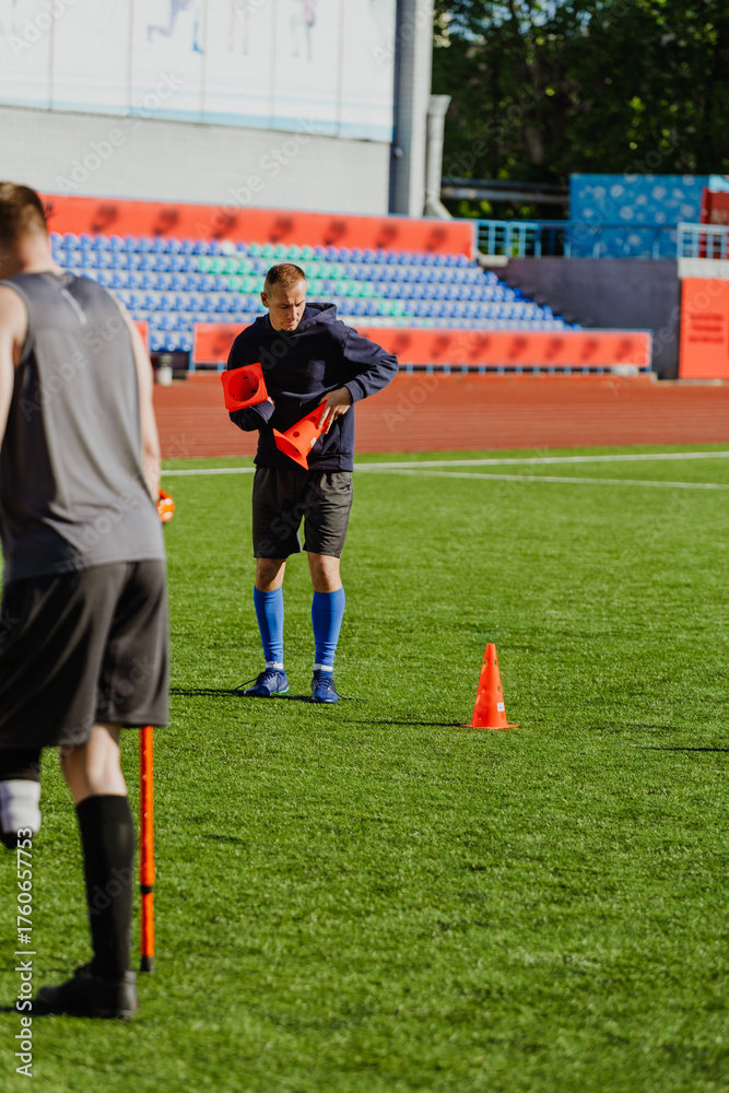 Fototapeta premium A man holds soccer cones and stands next to a man on crutches
