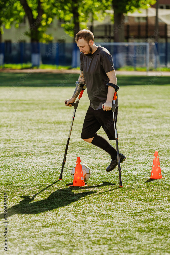 Fototapeta premium A man dribbles a ball between cones while leaning on crutches with his hands