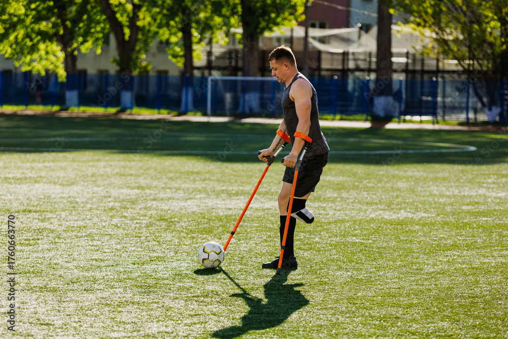 Obraz premium A man walks and dribbles a ball across the field with a crutch