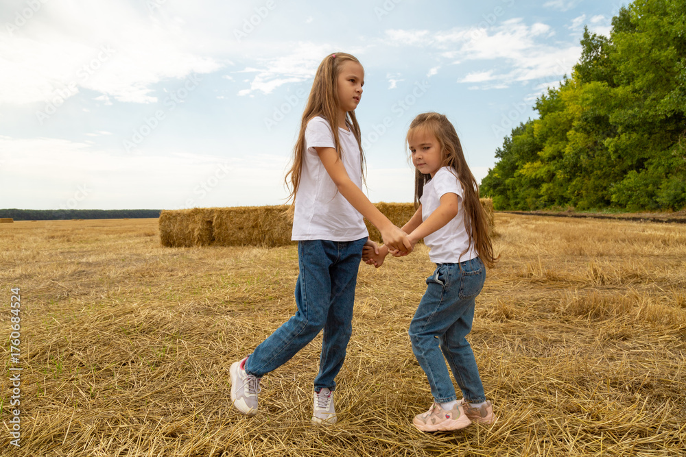 Fototapeta premium Children run on the mown wheat field where there are sheaves.