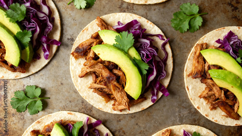 Tacos filled with shredded meat, avocado slices, purple cabbage, and cilantro on a rustic surface