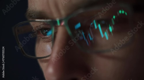Close up of focused crypto trader wearing glasses with stock market indexes reflecting in lenses while he analyzing cryptocurrency market in dark office. Trading and investment in crypto