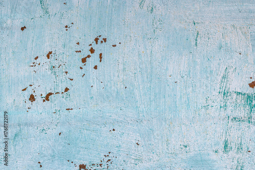 Grungy outdoor wall displays weathered light teal paint and patches of rust. Aged texture conveys rustic charm and character in a daytime setting.