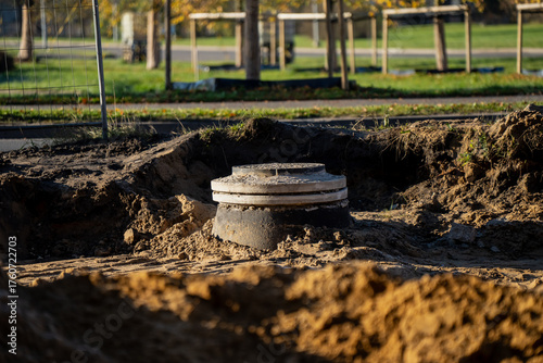 Newly installed concrete sewer manhole at construction site surrounded by excavated soil, part of underground water and drainage infrastructure installation in urban area