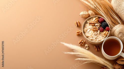 Warm bowl of oatmeal topped with nuts and berries sits beside cup of tea, surrounded by natural elements like dried grasses and nuts, creating cozy and inviting breakfast scene
