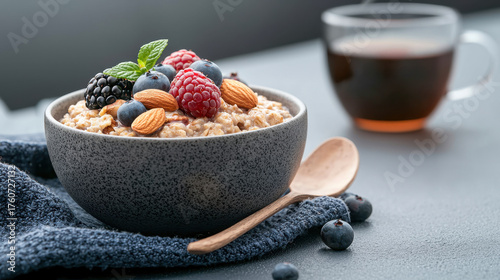 Healthy bowl of oatmeal topped with fresh berries, almonds, and mint, served with cup of tea in background. This nutritious breakfast is perfect for starting day with energy and vitality