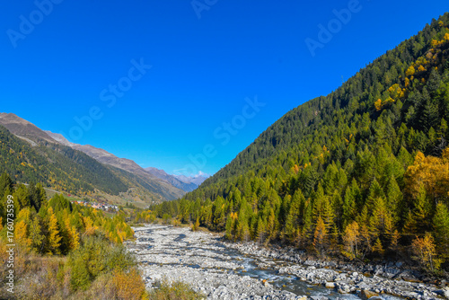 High mountain panorama in late summer, early autumn, with green and yellow larches, blue sky, in the Swiss Alps.