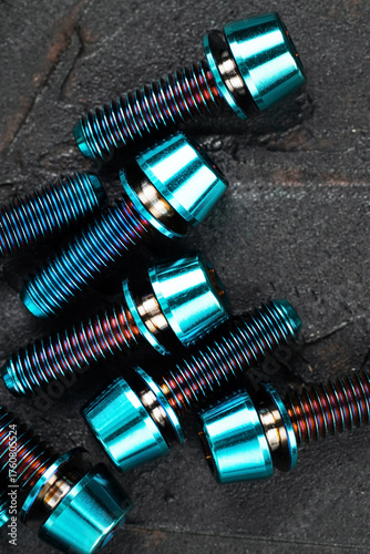 Screws made of blue-purple anodized titanium alloy on a black textured background