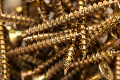 A close-up of a pile of shiny gold-colored wood screws with heads scattered randomly as a background