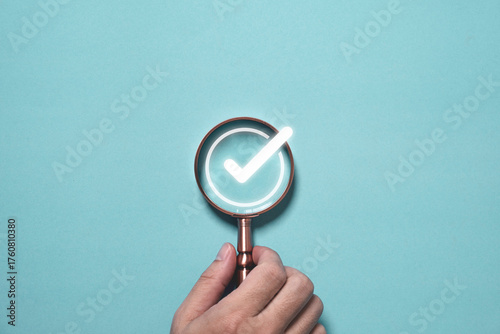 Hand holding magnifying glass focusing on glowing check mark symbol concept of approval quality control verification and successful inspection for business standard assurance and accuracy