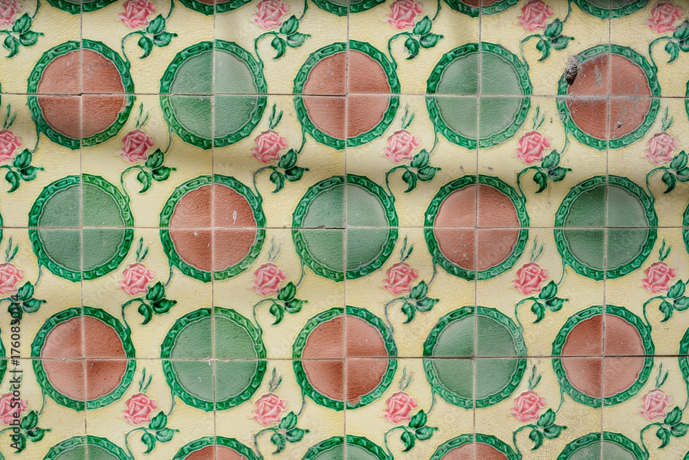 Antique majolica wall tiles featuring geometric pattern of green and pink medallions, rose, and cream background. This design reflects early 20th century lifestyle and aesthetic in Penang, Malaysia.