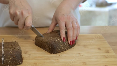 Woman is cutting a loaf of bread with a knife. The knife is on the left side of the bread