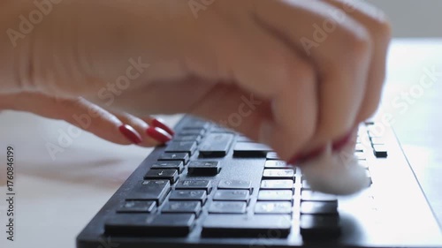 Woman is cleaning her keyboard with a cloth. The keyboard is black and has a white background