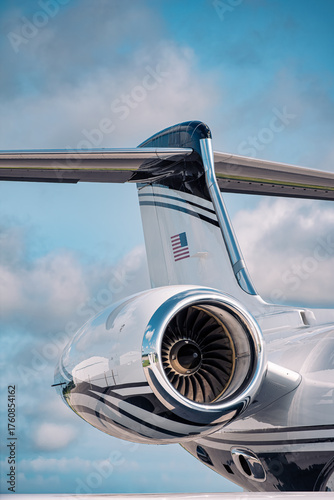 Turbofan engine and T-tail of a sleek business jet, showing aerodynamic precision and reflective metallic finish under a partly cloudy sky.