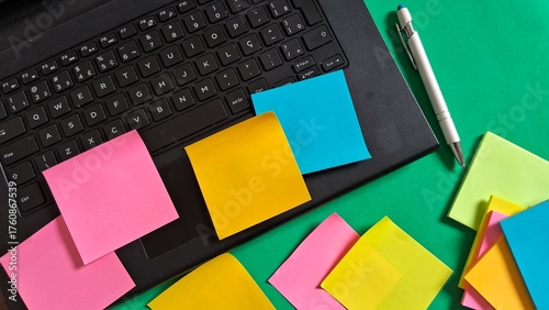Colorful sticky notes, pen and laptop on a green background