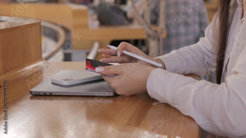 Person is writing on a laptop with a pen. The laptop is on a wooden table. The person is wearing a white shirt