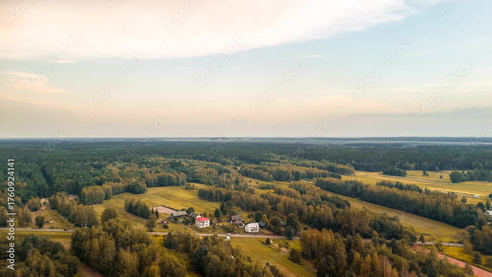 Fototapeta premium Aerial view of serene green landscape with fields and scattered houses under a soft evening light. Ideal for themes of nature, rural living, and tranquility.