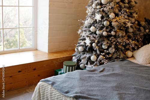 Cozy bedroom scene featuring a beautifully decorated Christmas tree adorned with ornaments and lights, soft bedding, and a warm window nook creating a festive atmosphere