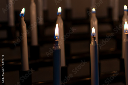 Low-light photo of several tall, white votive candles burning brightly in a church or sanctuary, creating a solemn and peaceful atmosphere