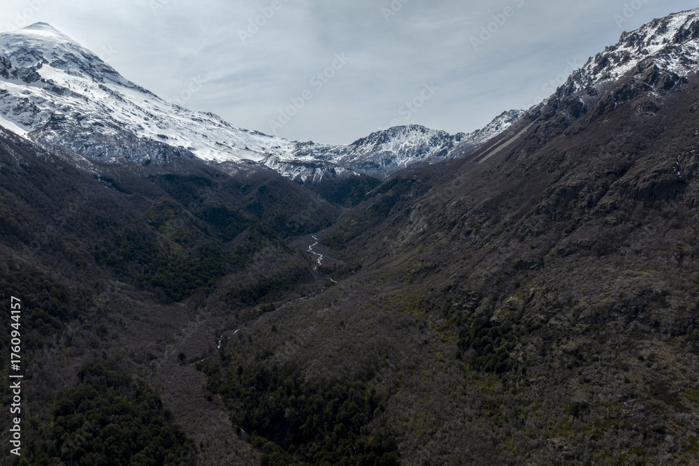 Fototapeta premium Deep Mountain Valley with a Small Stream and Snow Capped Peaks