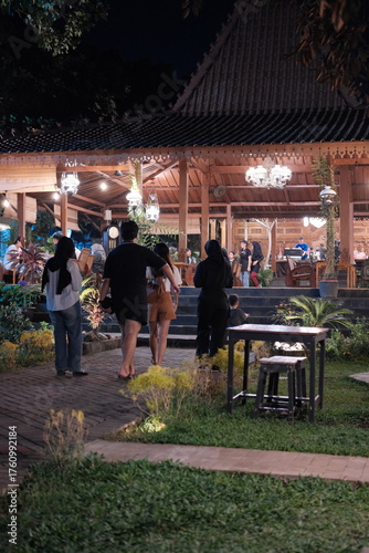 Experience the vibrant atmosphere of an outdoor restaurant at night, where people gather to enjoy good food and good company under the soft glow of lights