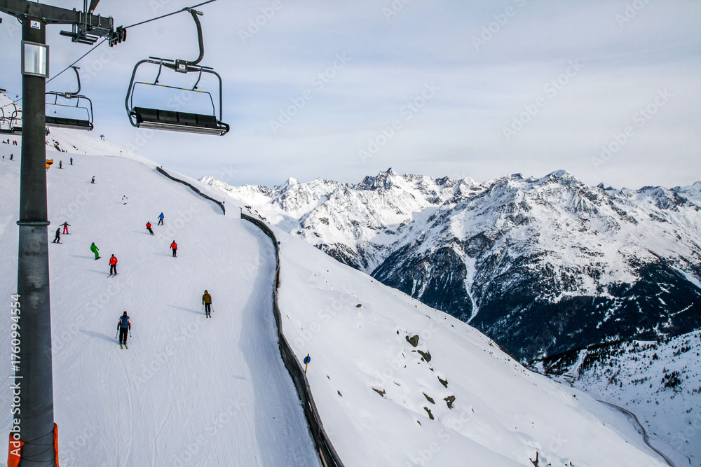 Obraz premium Skiers on a snowy slope with a chairlift and alpine mountains in winter