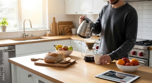 Man making coffee in a modern kitchen with fresh fruit and bread on the counter.