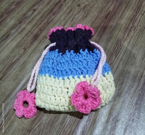 Handmade crocheted drawstring pouch in bright pastel colors with floral appliqués, resting on a wooden surface.