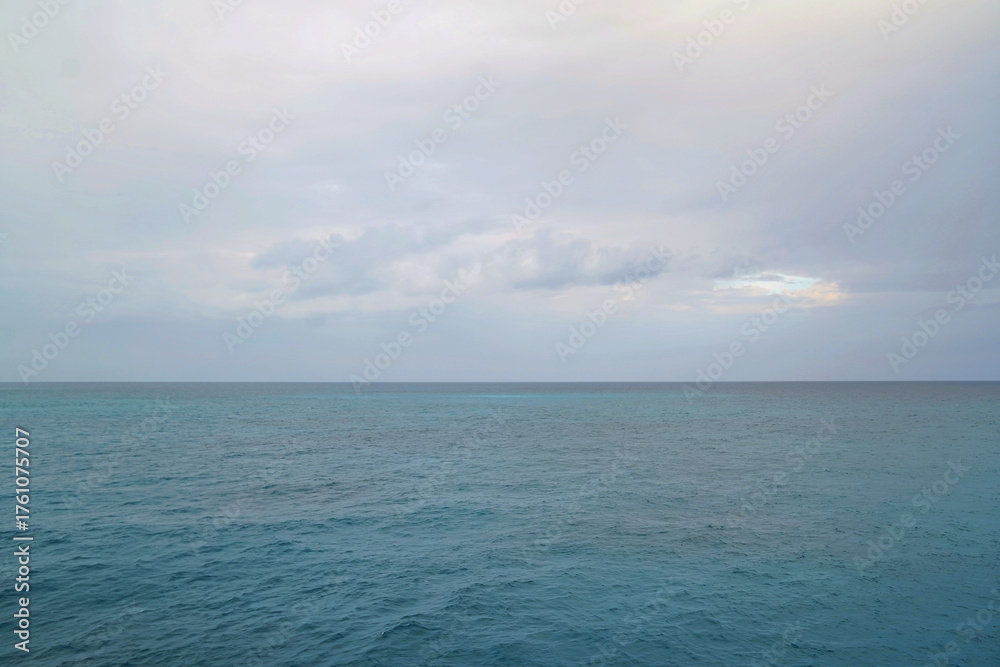 Obraz premium Expansive view of the Caribbean Sea under a soft, overcast sky, highlighting layers of blue and gentle waves, captured from a Royal Caribbean Cruise during calm tropical weather