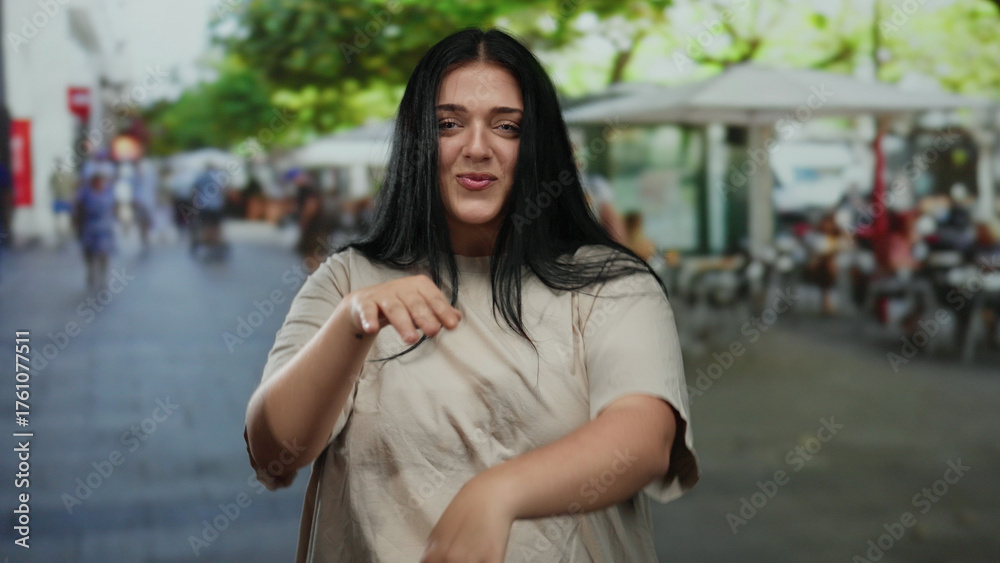 Fototapeta premium Young plus size woman joyfully dancing with a smile on a lively city street filled with outdoor cafes and trees, showcasing her curvy beauty in a bustling urban environment.