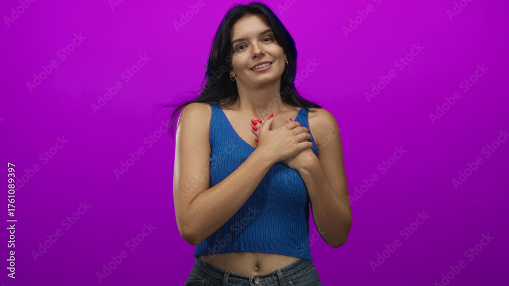 Naklejka premium Young hispanic woman wearing blue tank top and jeans smiling and clutching chest in studio; gratitude.
