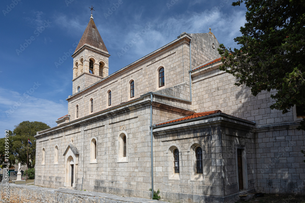 Naklejka premium Stone Church With Bell Tower Surrounded by Green Trees Against a Blue Sky, Grohote, Solta