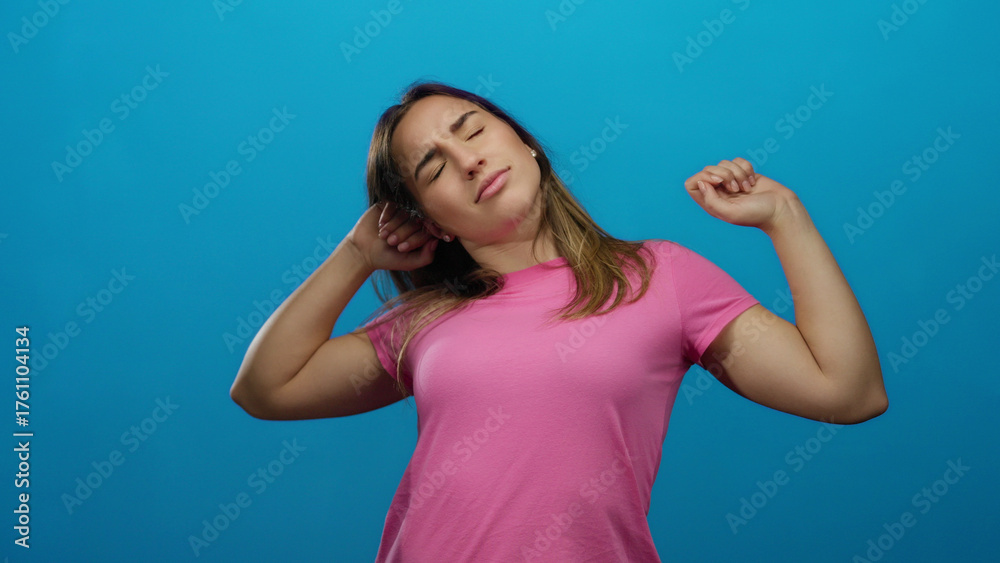 Fototapeta premium Woman stretching with closed eyes isolated on a bright blue background, expressing relaxation, wearing a pink shirt, blonde hair, young adult, peaceful, casual expression.