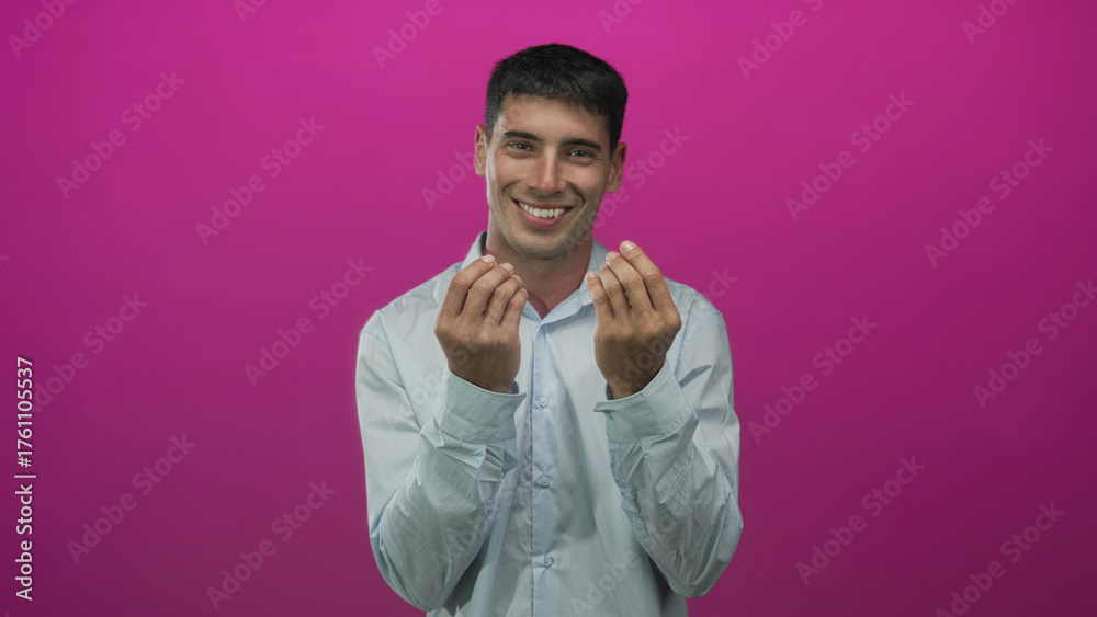 Obraz premium Young hispanic man holds both hands in money gesture against a pink studio wall; playfulness prosperity.