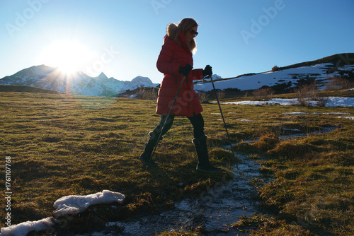 Woman hiking mountains using trekking poles at winter sunset