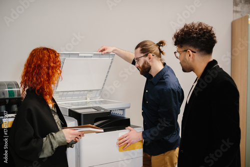 Office colleagues collaborating on printing documents using a copier machine