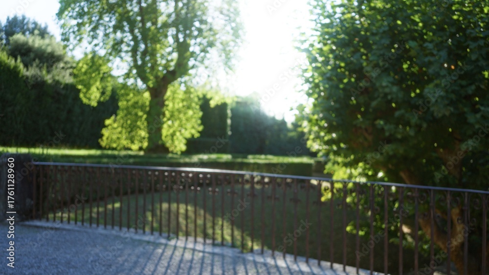 Obraz premium Blurred scene with soft bokeh and defocused iron railing under sunlit trees in a garden, shallow focus outdoor; background copyspace calm.