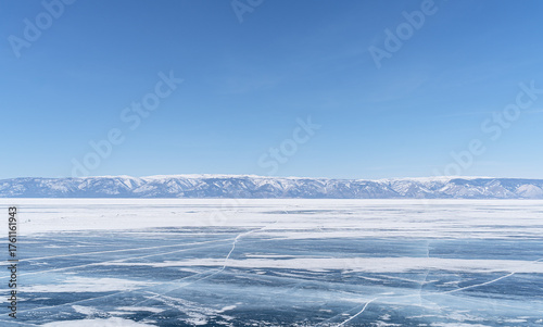 Expansive frozen lake landscape with clear blue sky and distant snow-capped mountains
