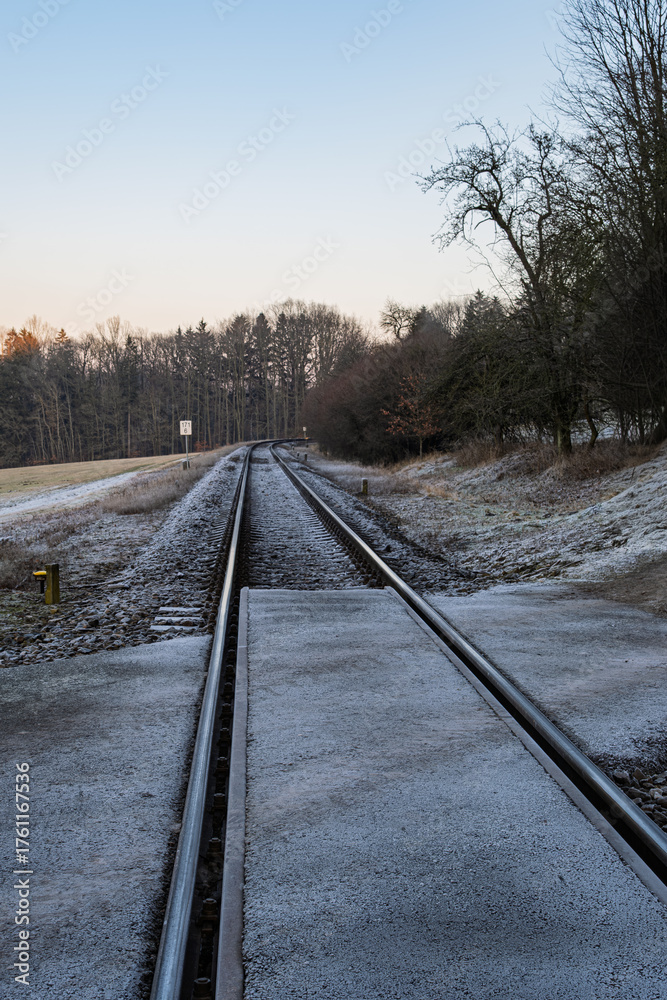 Fototapeta premium Railway crossing covered with frost leading into forest and open countryside on a cold winter morning.