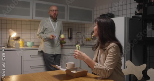 Side view girl in business clothes office worker holding sandwich in hands and talking with her colleague guy who leaned on kitchen counter During lunch in office kitchen