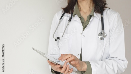 Quadro su tela Unknown professional woman doctor, wearing white coat over a green blouse and a stethoscope, is using a digital tablet, suggesting innovative healthcare practices in medicine