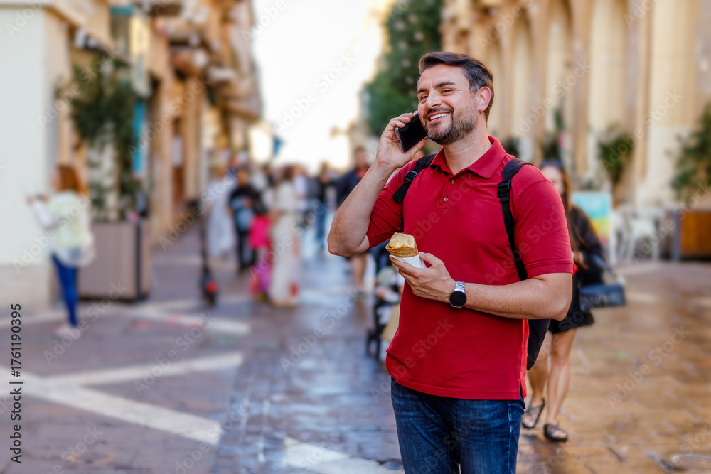 Fototapeta premium Man enjoying pastry while talking on phone in busy street during daytime